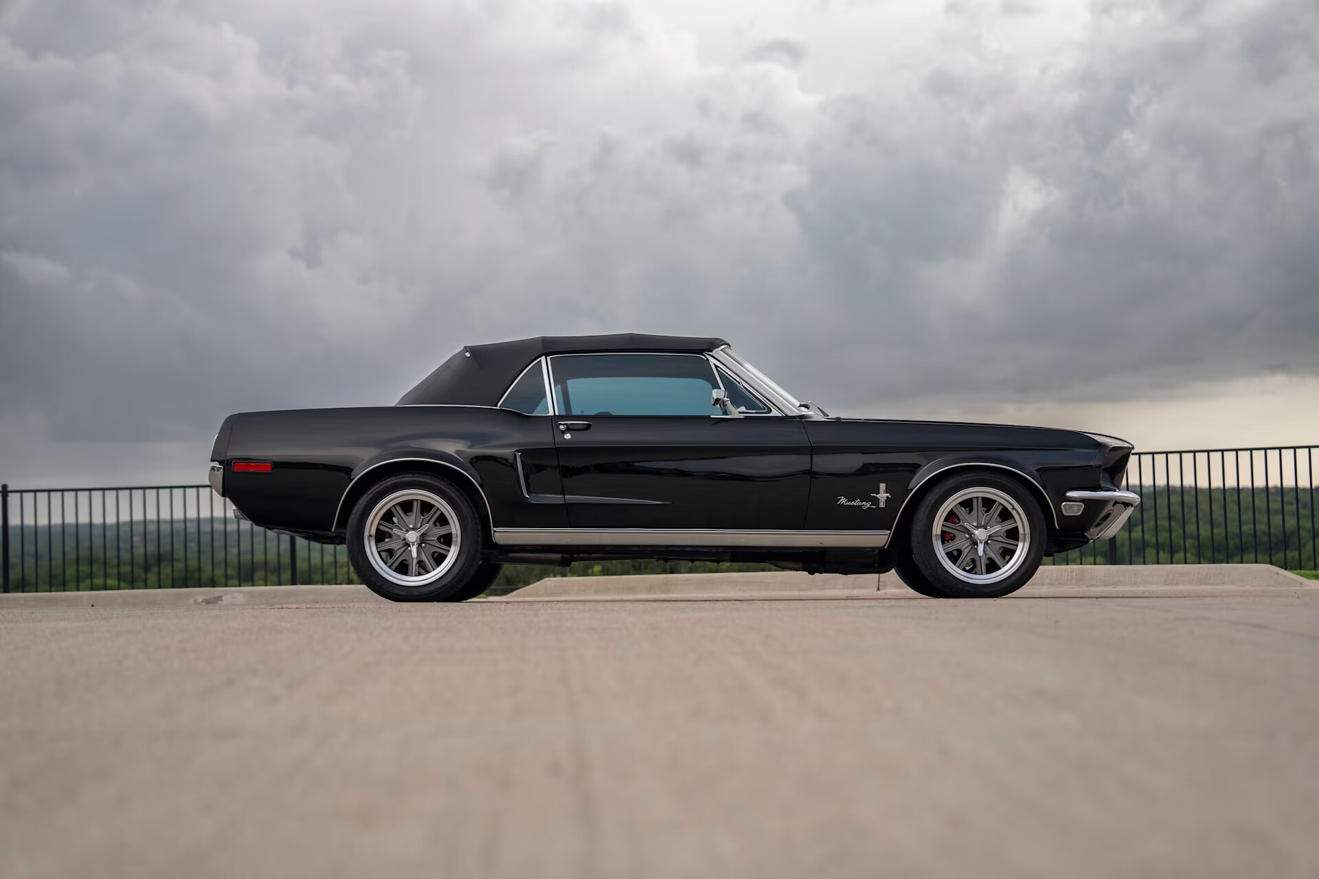 Side profile of the triple-black 1968 Mustang convertible under Texas storm clouds